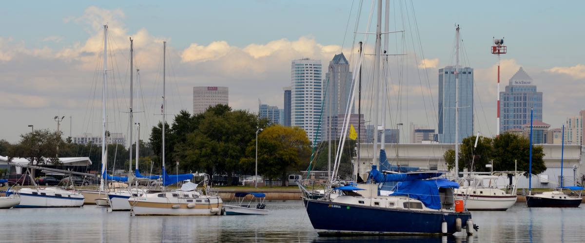 Sailboats moored in the Davis Islands yacht basin, with the downtown Tampa skyline and scattered clouds behind them.