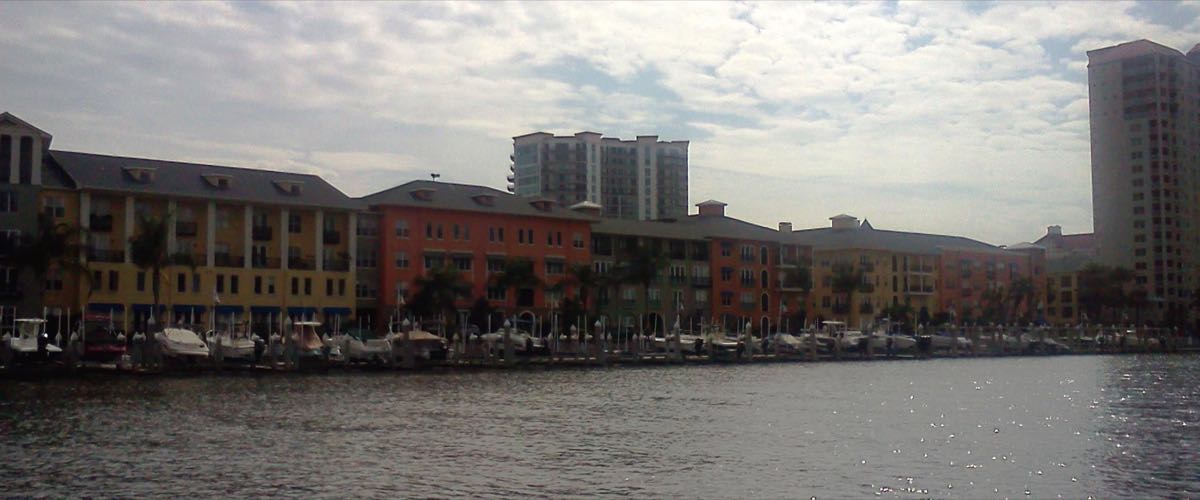 Waterfront condominium buildings and a marina full of docked boats on Harbour Island, Tampa, seen across the water on a partly cloudy day with the downtown Tampa skyline in the background.
